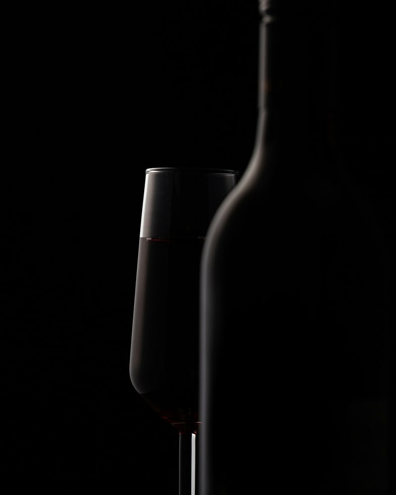 Photographie d’illustration : une bouteille et un verre de vin sur fond sombre